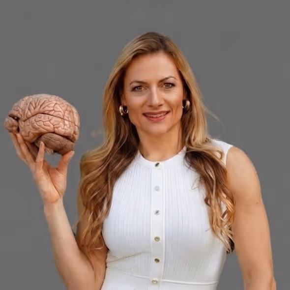 Smiling woman in white dress holding a model of a human brain against gray background.