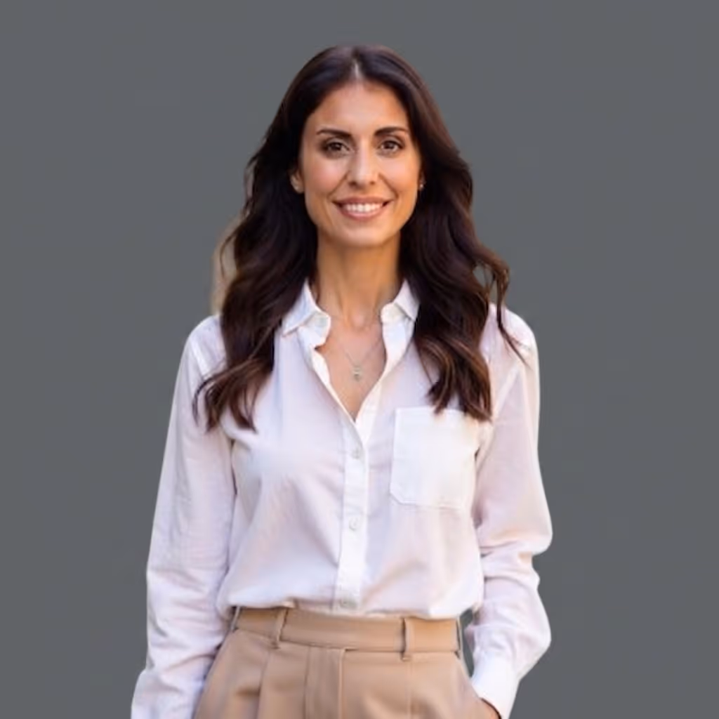 Smiling woman with long dark hair wearing a white button-up shirt and tan pants on gray background.