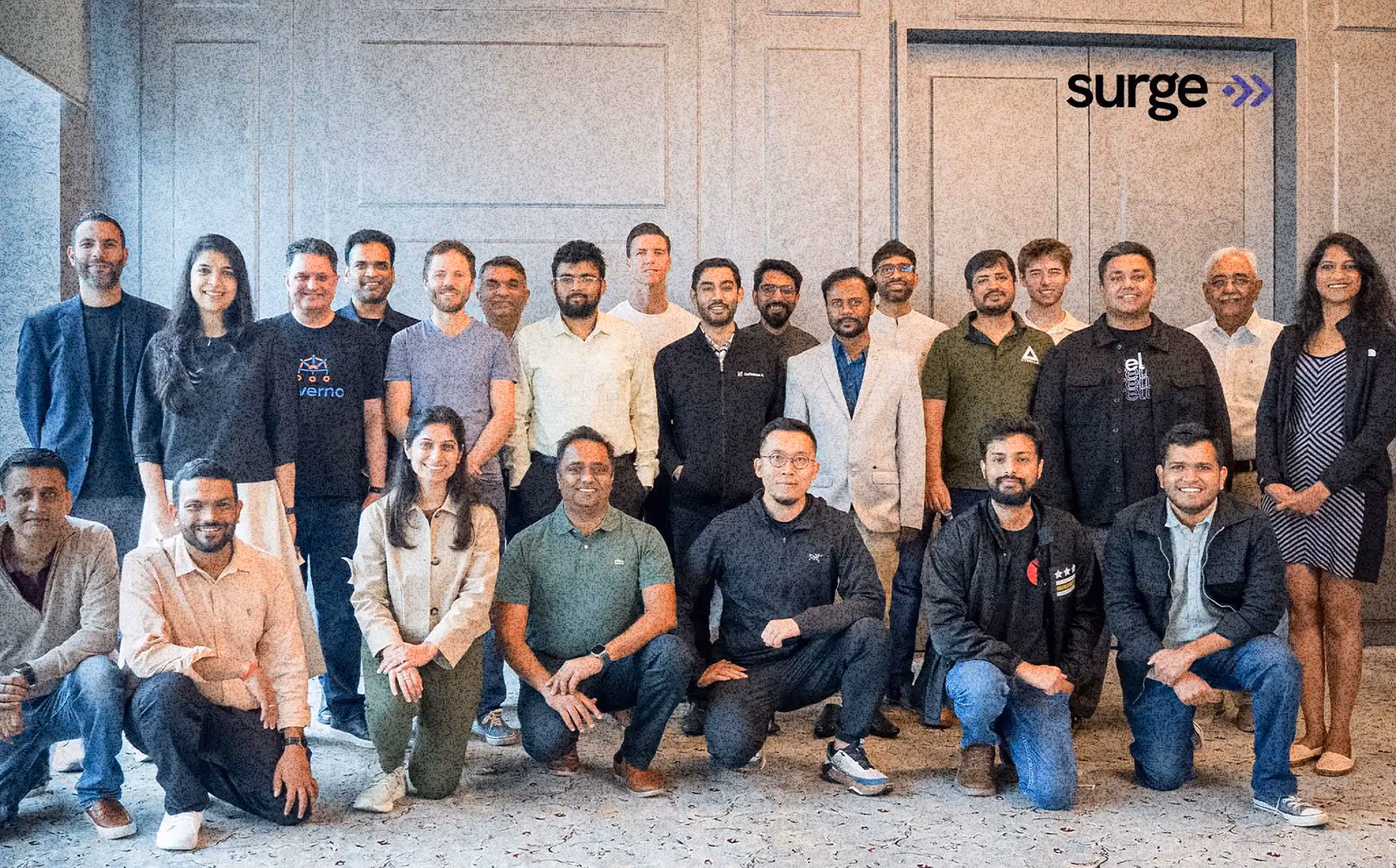 Group photo of 24 diverse professionals posing indoors in front of a wall with the word surge.