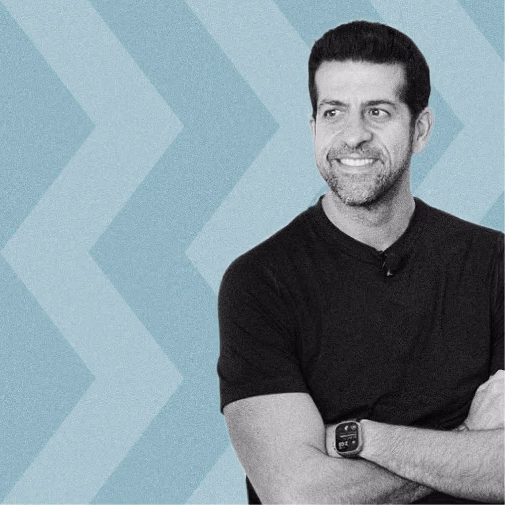 Smiling man with crossed arms wearing a black t-shirt and smartwatch against blue chevron background.