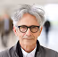 Older man with white hair and glasses smiling outdoors.