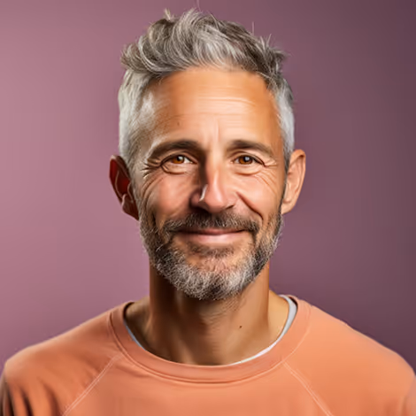Smiling middle-aged man with gray hair and beard wearing a peach sweatshirt against a purple background.
