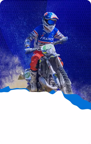 Motorcyclist in France gear riding a dirt bike against a blue background kicking up dust.