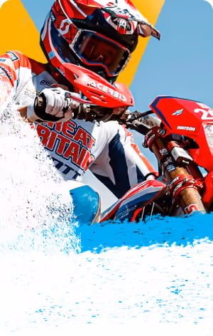 Motorcyclist in red, white, and blue gear riding off-road against a blue sky and yellow background.