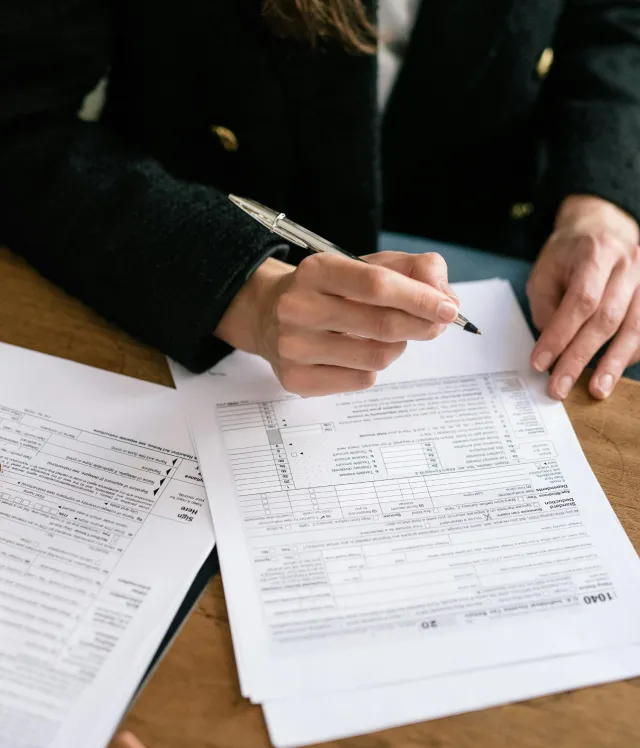 Person holding a pen and filling out tax forms on a wooden table.