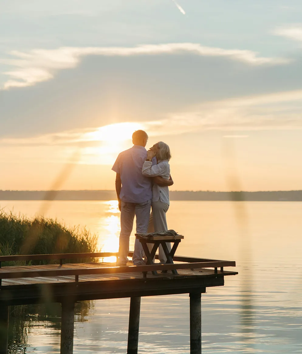 A couple embracing on a wooden dock overlooking a calm lake during sunset.