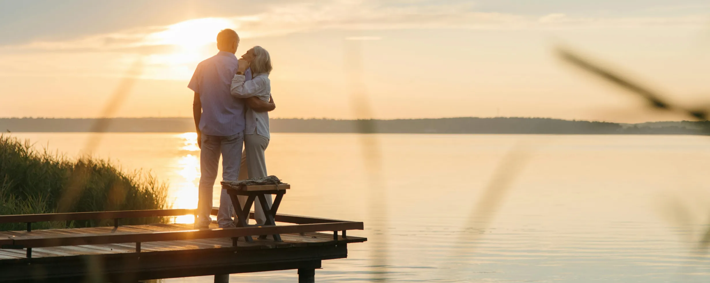A couple embraces on a wooden dock overlooking a calm lake at sunset.