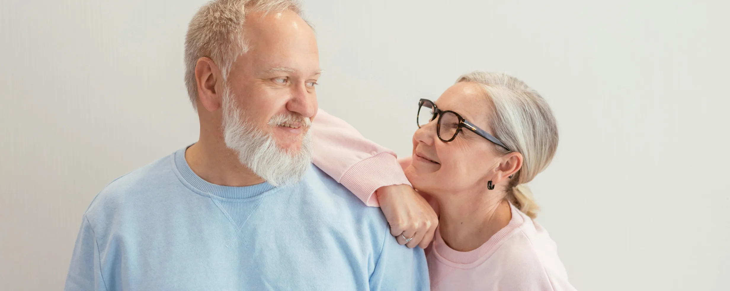 Elderly couple smiling and looking at each other, with the woman resting her arm on the man's shoulder.