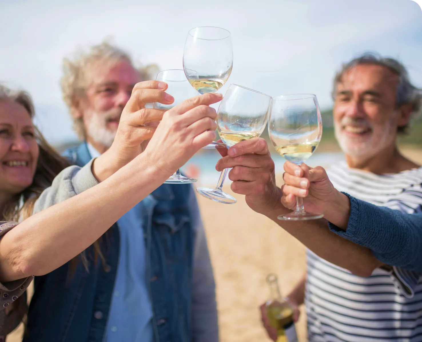 Group of older adults clinking glasses of white wine together outdoors on a sunny day.