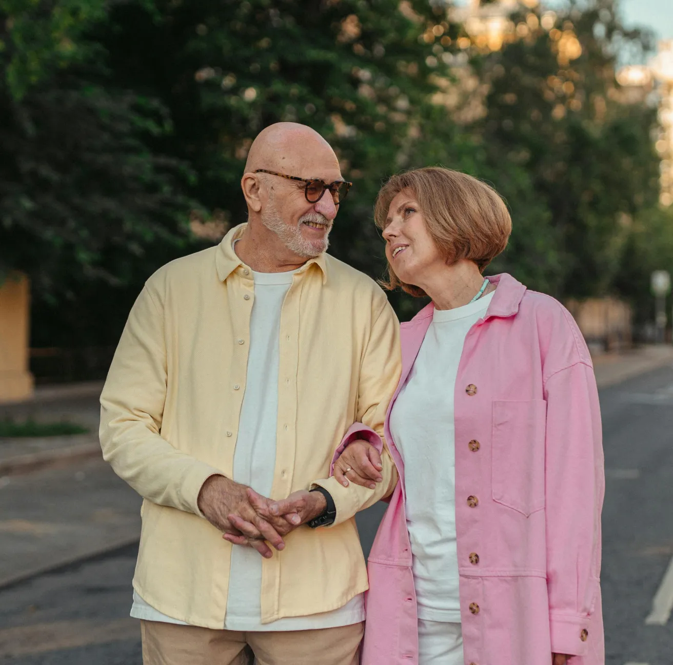 Smiling elderly couple walking outdoors with the woman linking arms with the man.
