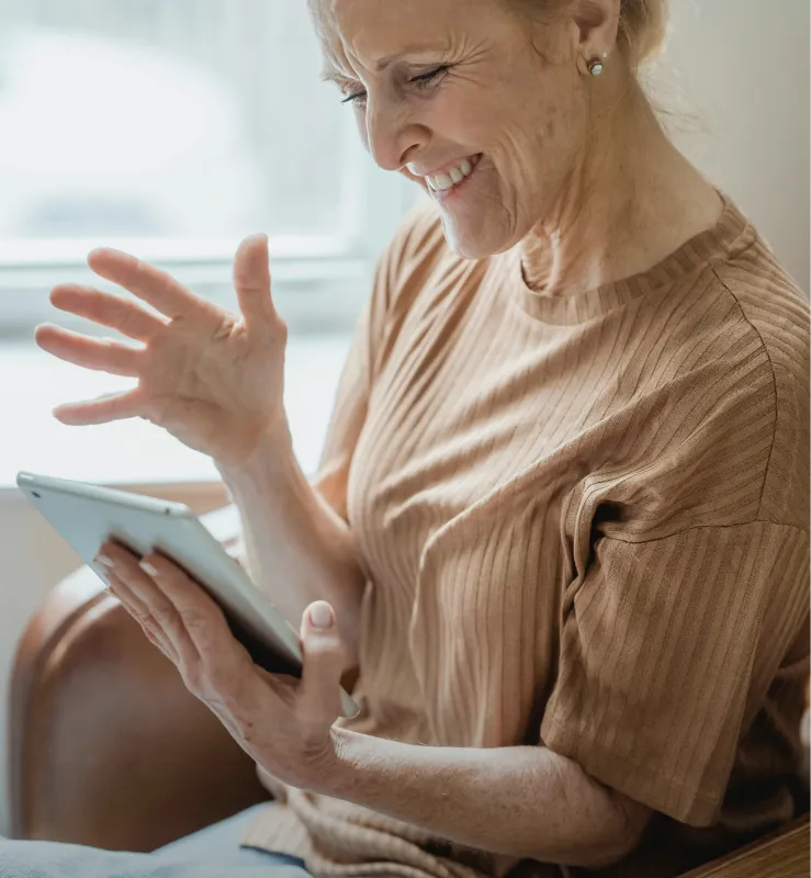 Smiling elderly woman waving and looking at a tablet screen.