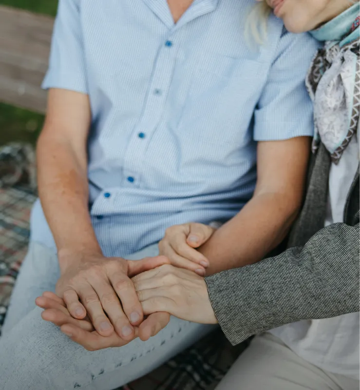 Two people sitting closely with one resting their head on the other's shoulder and holding hands.