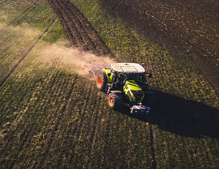 Aerial drone shot of a green tractor tilling a field at sunset with dust rising