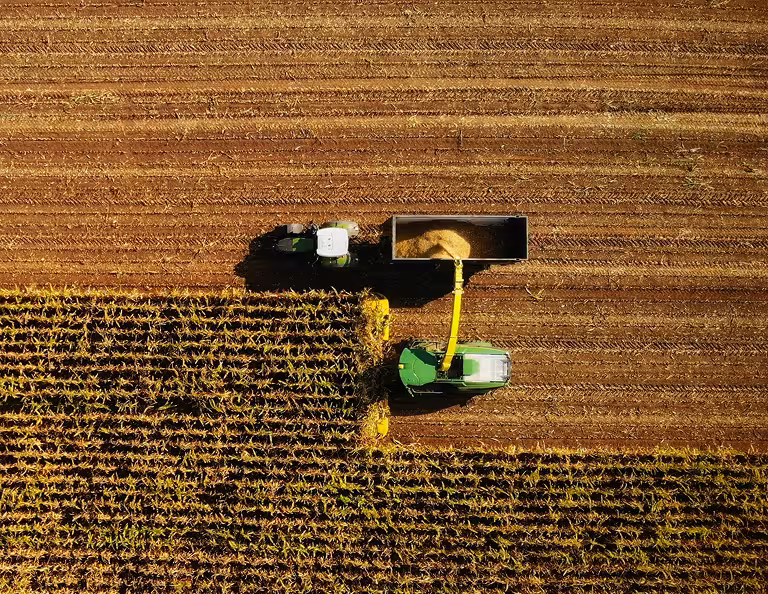 Top-down aerial view of a combine harvester offloading grain into a trailer on a harvested field