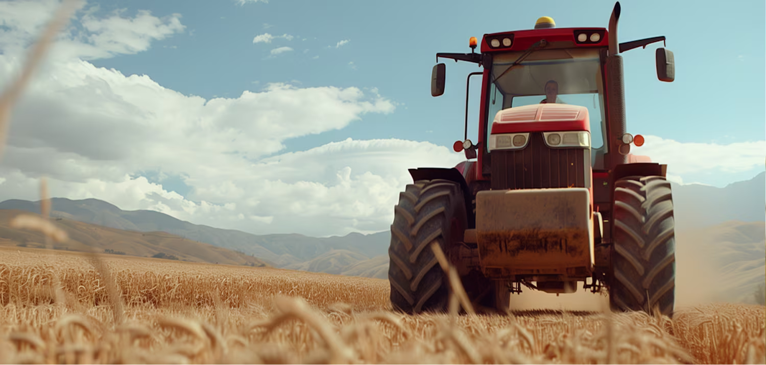 Front view of a large red tractor standing in a golden wheat field under a bright blue sky with mountains