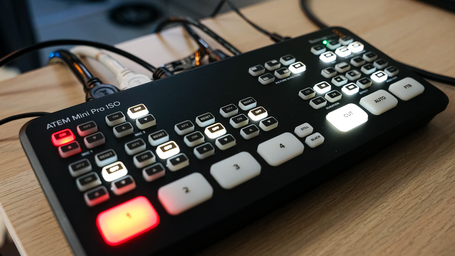 ATEM Mini Pro ISO video switcher on a wooden surface with several illuminated buttons and cables.