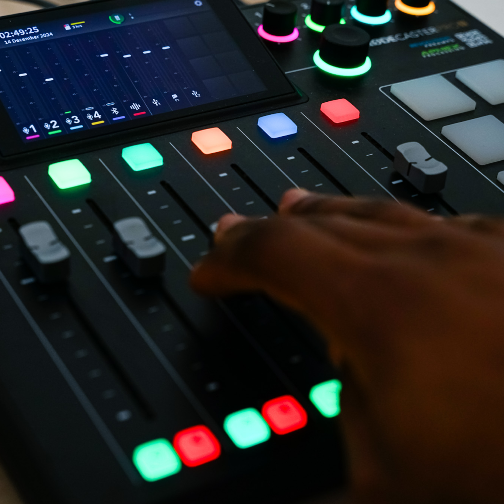 Hand adjusting sliders on a digital audio mixing console with colorful illuminated buttons and display.