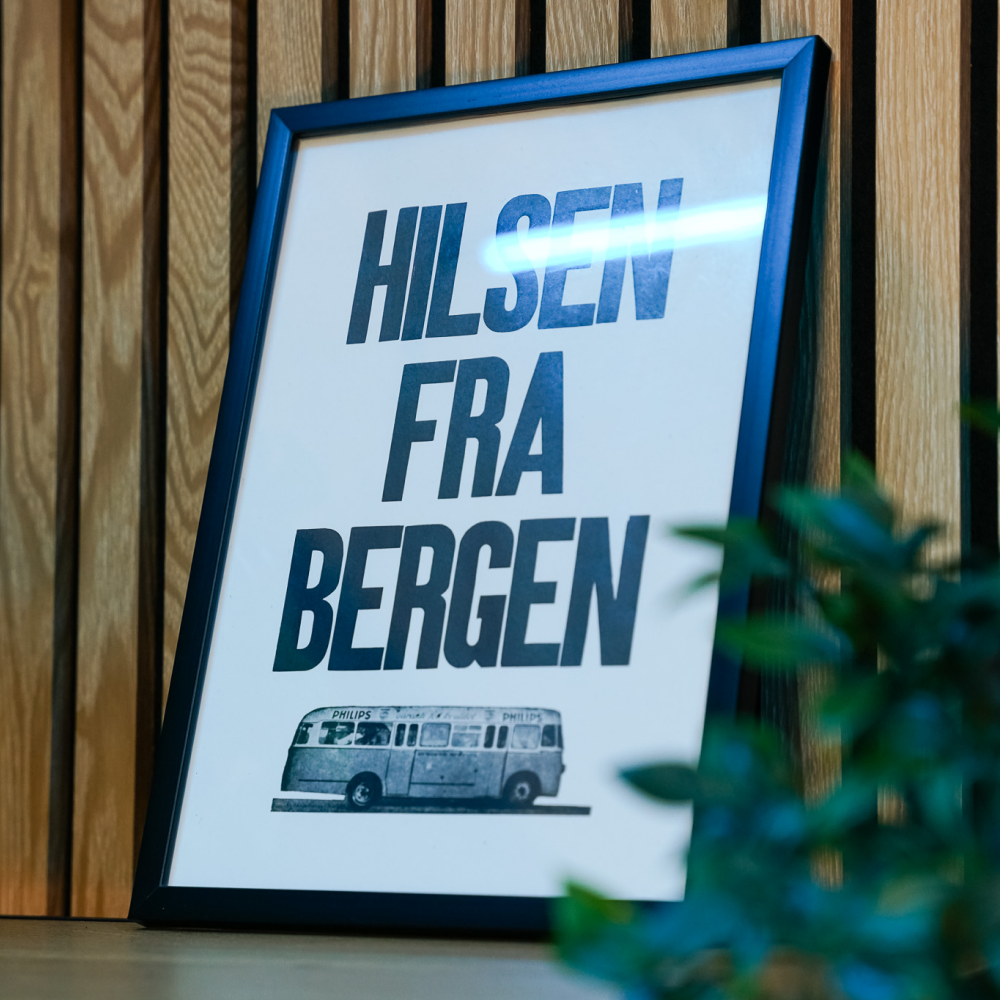 Framed sign reading 'Hilsen Fra Bergen' with a vintage bus illustration below it.