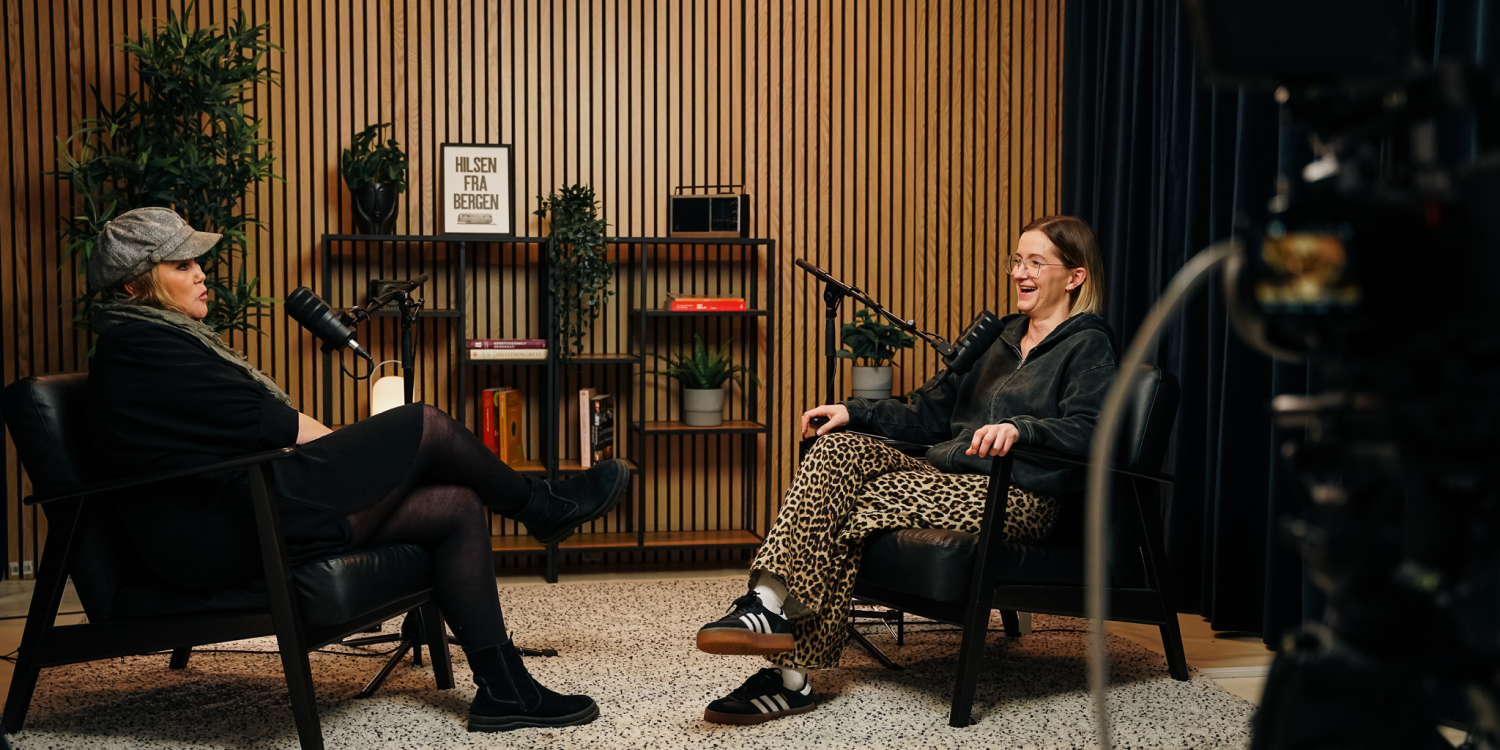 Two women seated facing each other in a podcast studio with microphones and a camera visible.