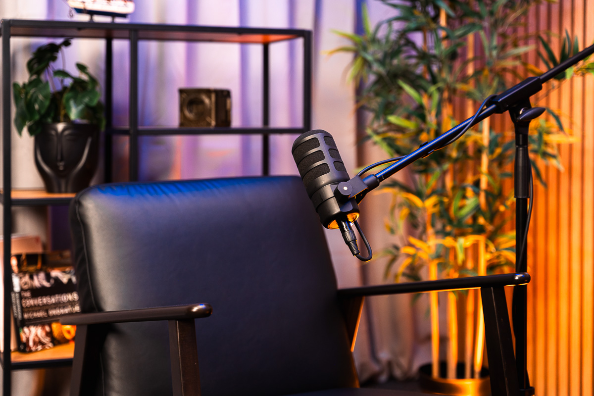 Black leather chair with podcast microphone on stand in cozy room with plants and shelves.