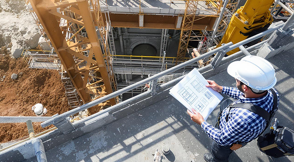 Ein Polier steht auf einer Baustelle und hält einen Bauplan in der Hand.