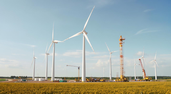 Mehrere Windräder stehen auf einem großen Feld unter blauem Himmel.