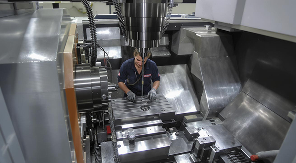 Ein Mann steht an einer CNC Fräse und bearbeitet Metall.