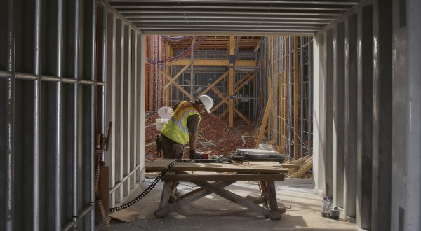 Ein Bauarbeiter steht in einem Baucontainer und lehnt sich auf einen Arbeitstisch.
