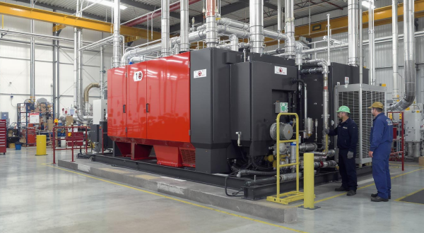 Rote Industrieanlage mit Rohrsystem und Arbeitern in einer Fabrikhalle.