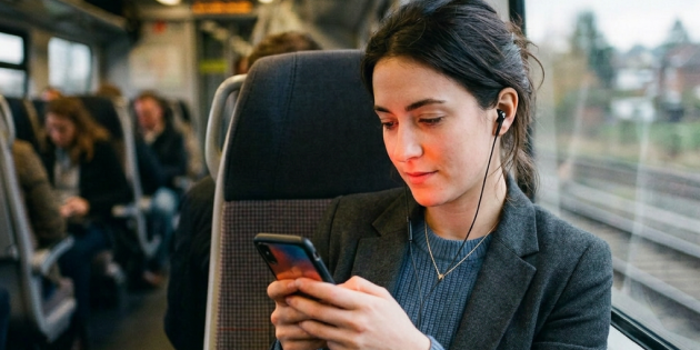 Eine Frau sitzt im Zug und schaut konzentriert auf ihr Handy.