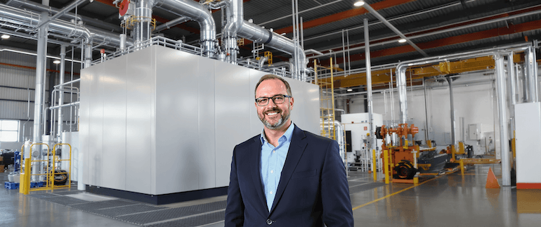 Ein Mann im Anzug steht vor einem Blockheizkraftwerk.