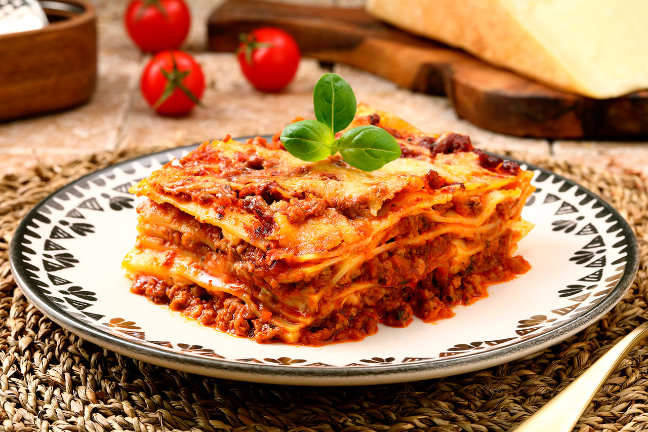 Slice of layered lasagna with meat sauce and cheese garnished with basil on a decorative plate.