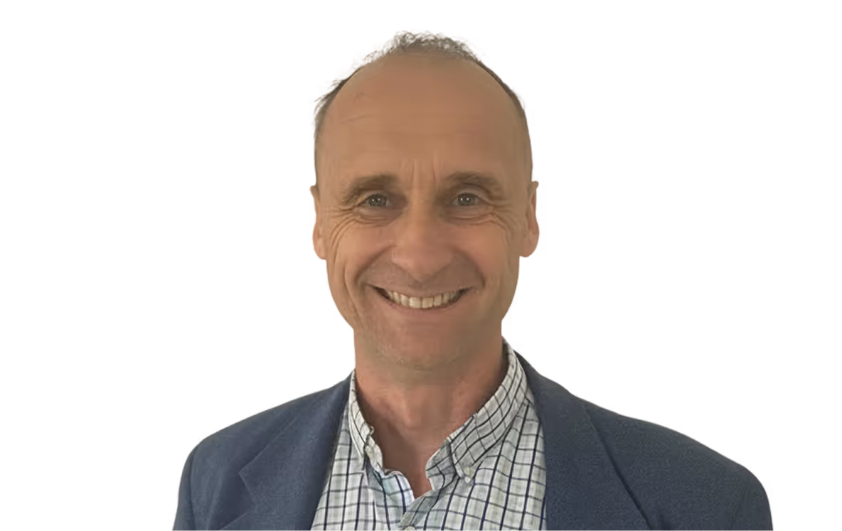 Smiling middle-aged man with short hair wearing a checkered shirt and dark jacket against a plain light background, the man is Renaud COUCHET.