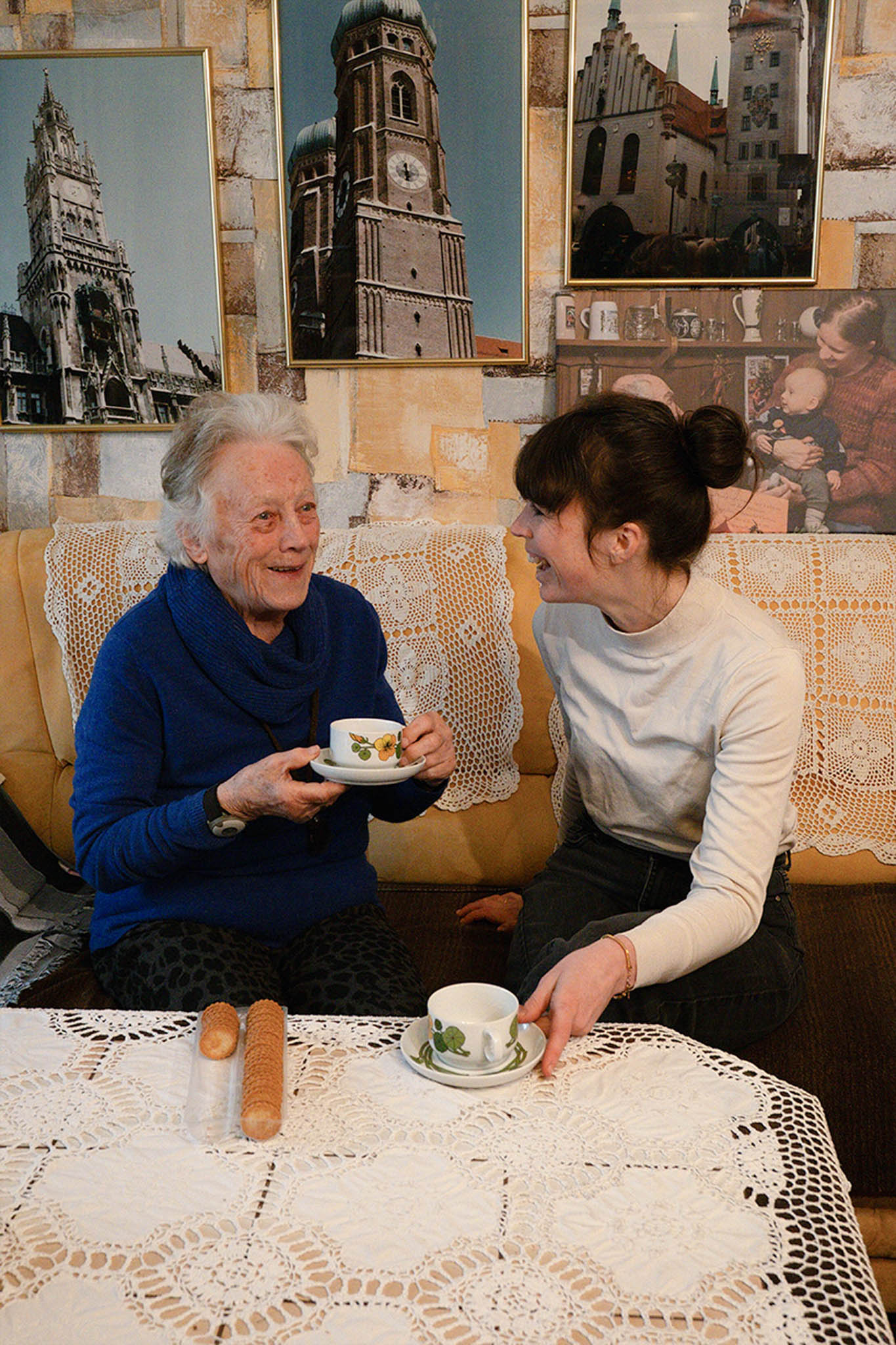 Ältere Frau und jüngere Frau sitzen und trinken gemeinsam Kaffee auf dem Sofa.