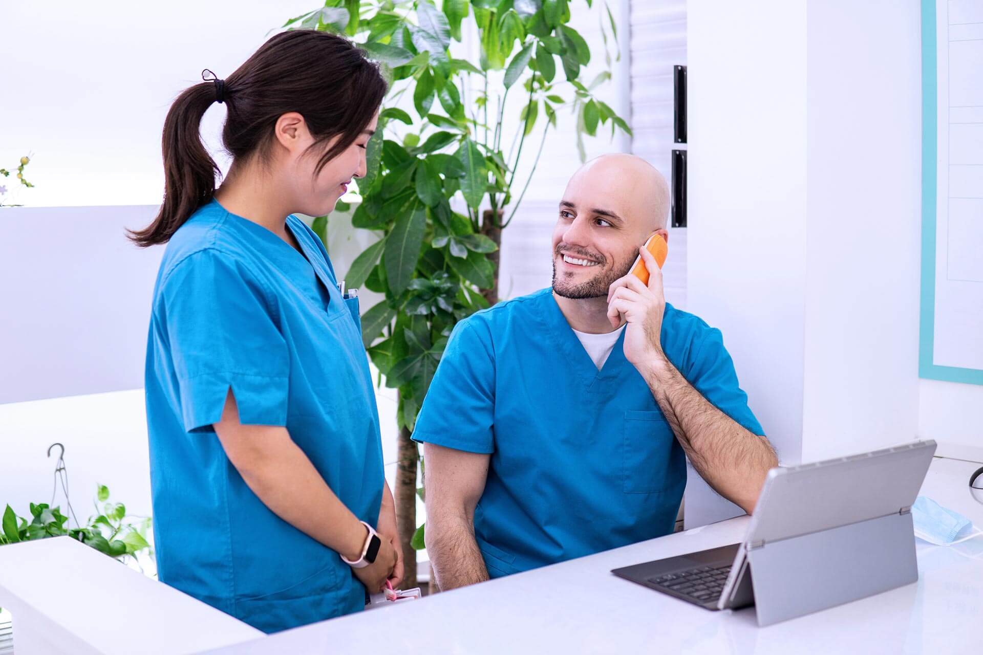 A man in scrubs talking on a cell phone next to a woman in scrub.