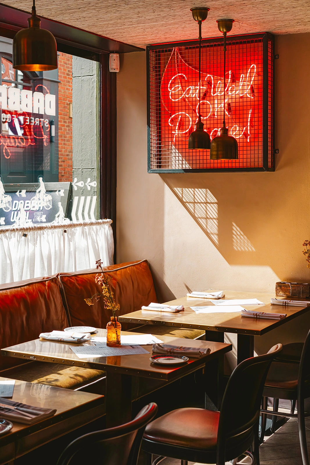 Sunlit window seating and red neon sign inside Dabbawal Indian street food restaurant, Newcastle