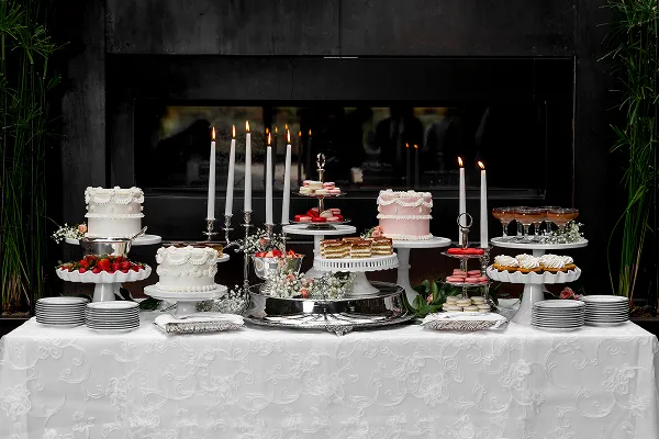 A dessert table spread by Bartleby & Sage, featuring cakes, cupcakes, macarons, and mousse cups arranged around taper candles