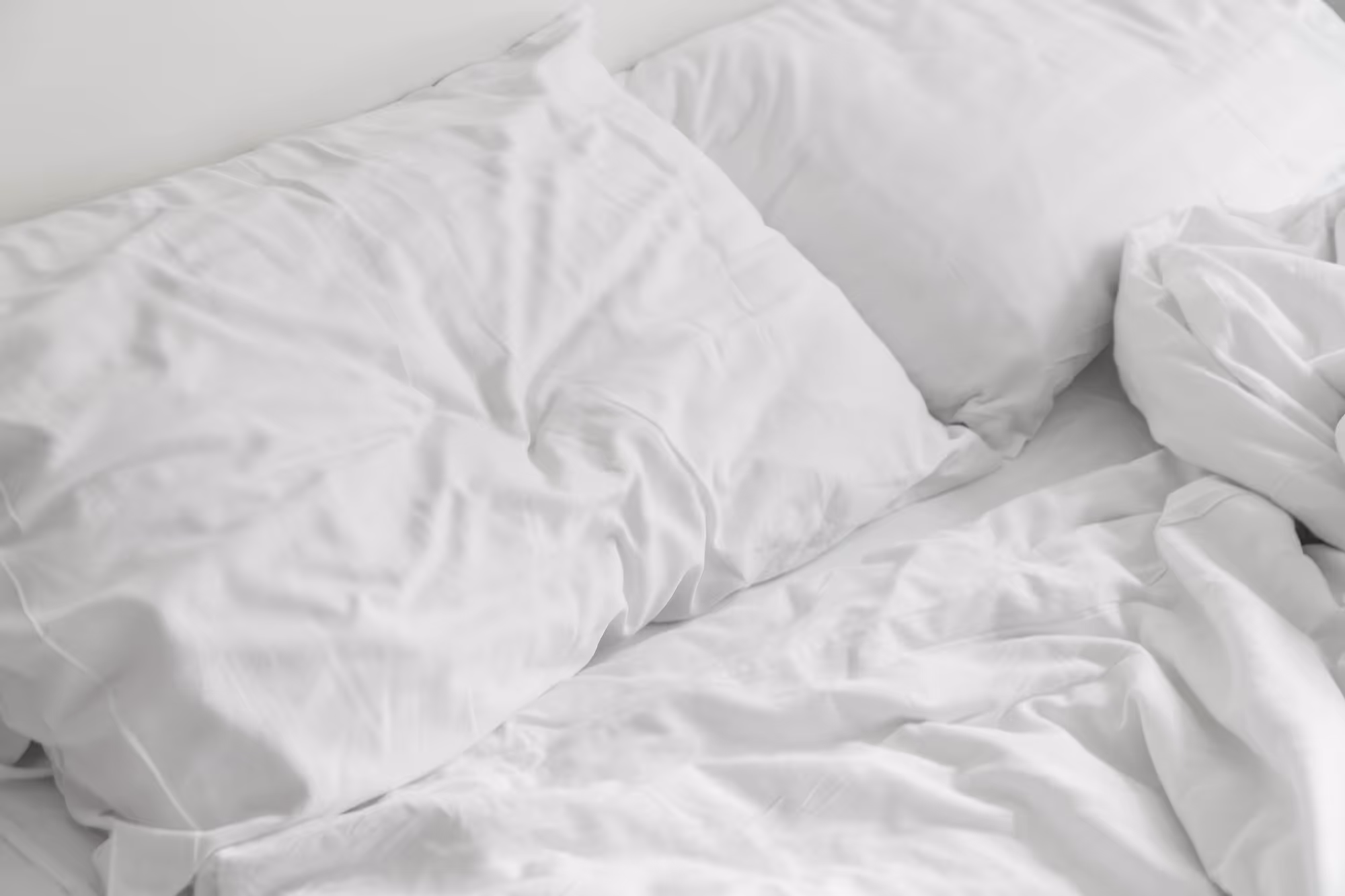 Crumpled white bed sheets and pillows on an unmade bed.