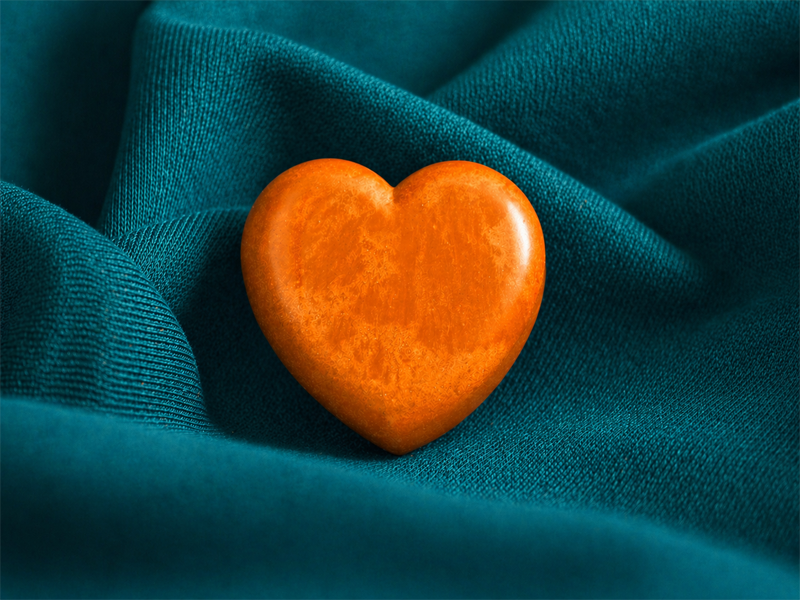 Orange heart-shaped stone resting on textured teal fabric.