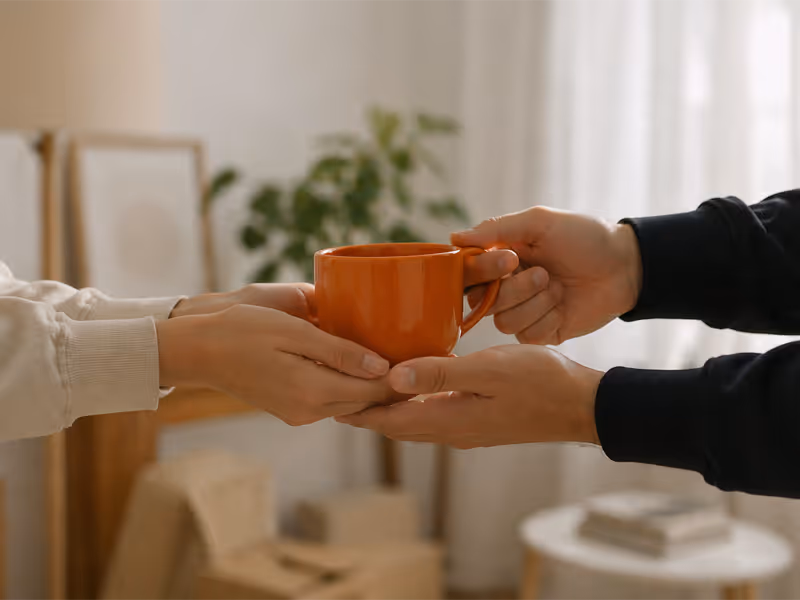 Two people exchanging an orange ceramic mug indoors with blurred background.