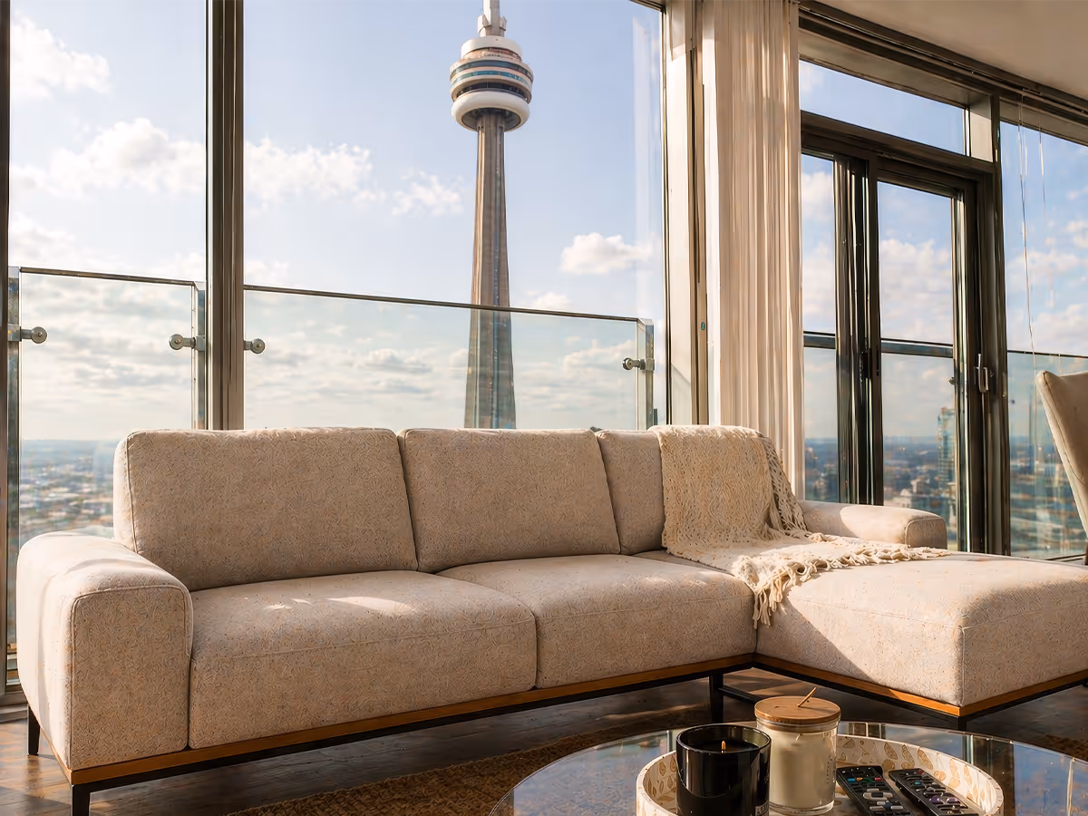 Beige sectional sofa with a throw blanket by large windows showing cityscape and tower view.