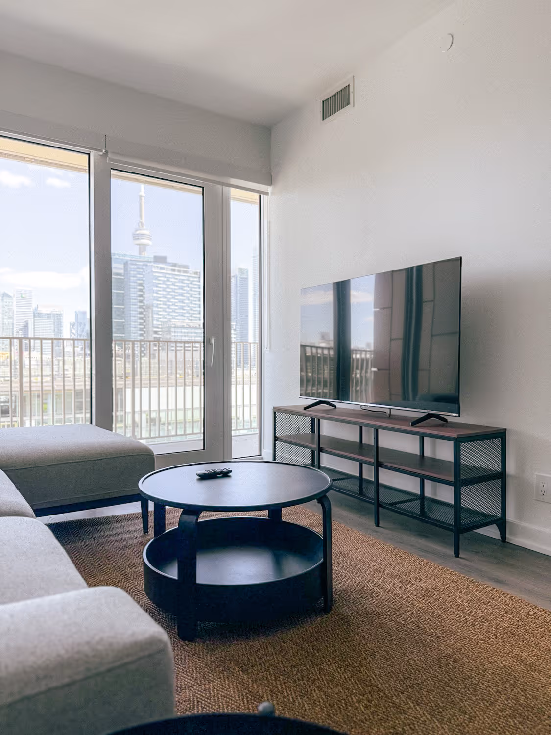 Modern living room with gray couch, round black coffee table, TV on stand, and city skyline view.