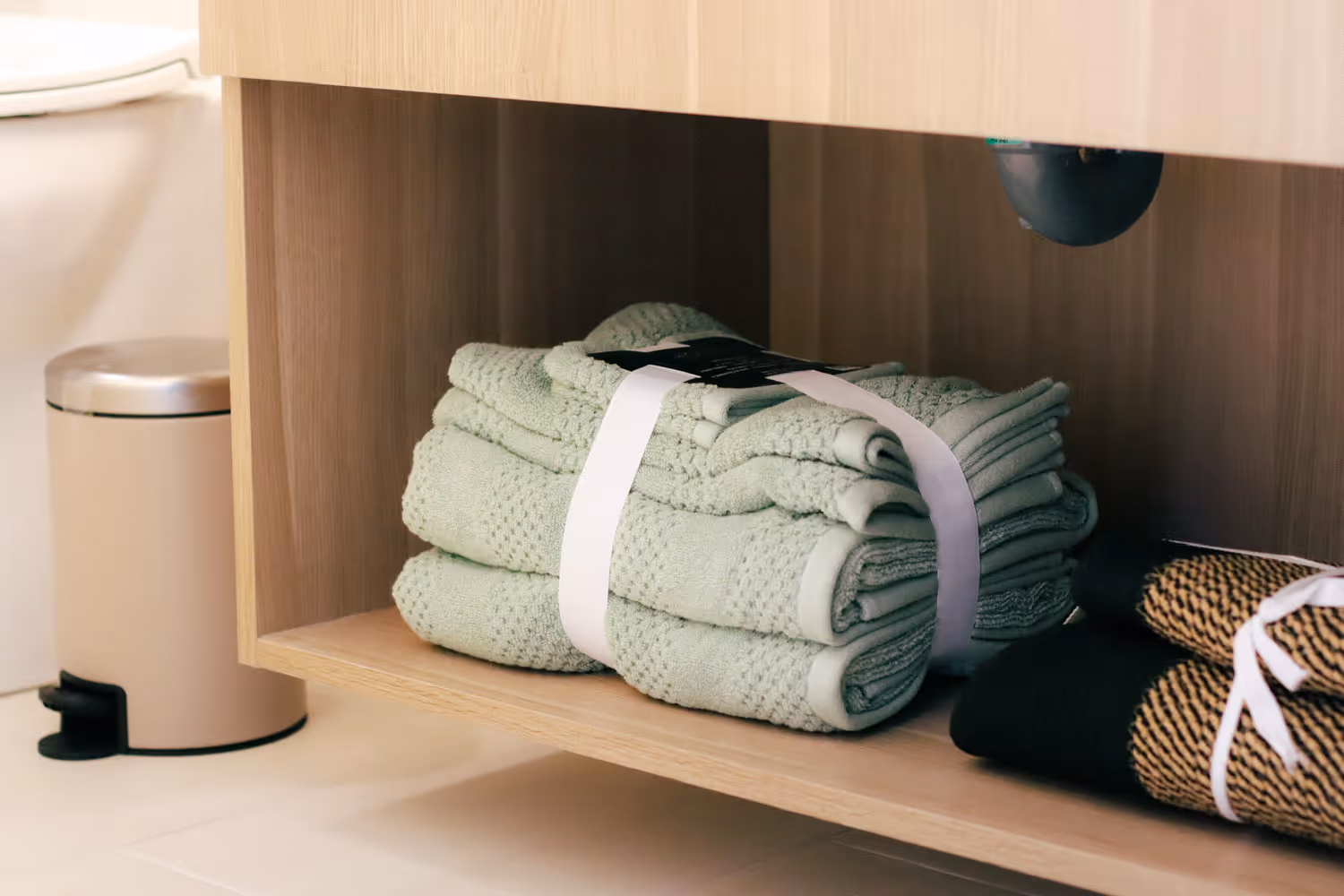 Folded green and black towels stacked neatly on a wooden shelf under a bathroom sink.