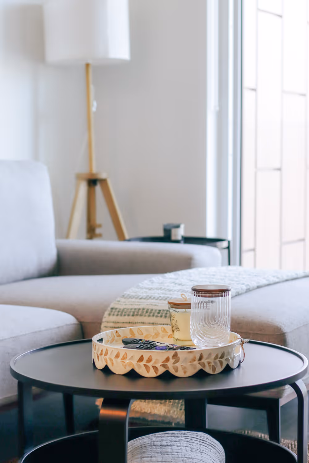 Black round coffee table with decorative tray, remote, candle, and glass in a modern living room.