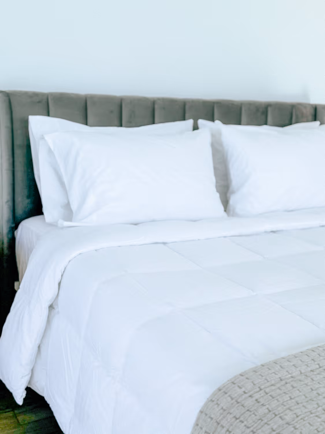 Neatly made bed with white pillows, white comforter, and gray velvet upholstered headboard.