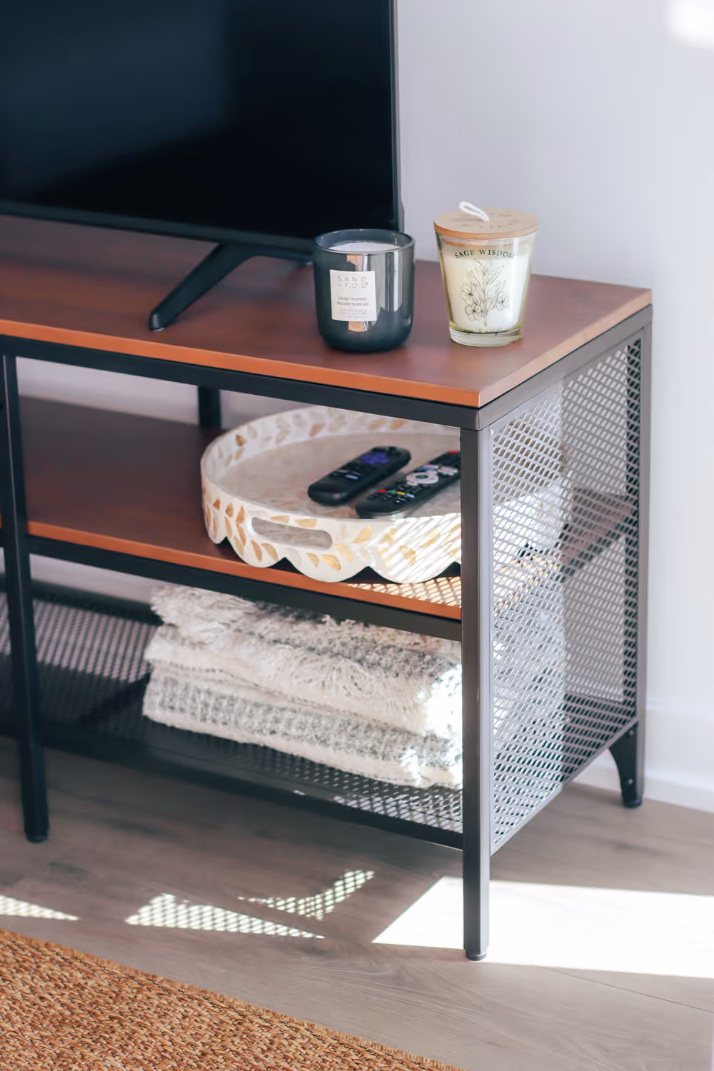 TV stand with two candles, a tray holding remote controls, and folded blankets on bottom shelf.
