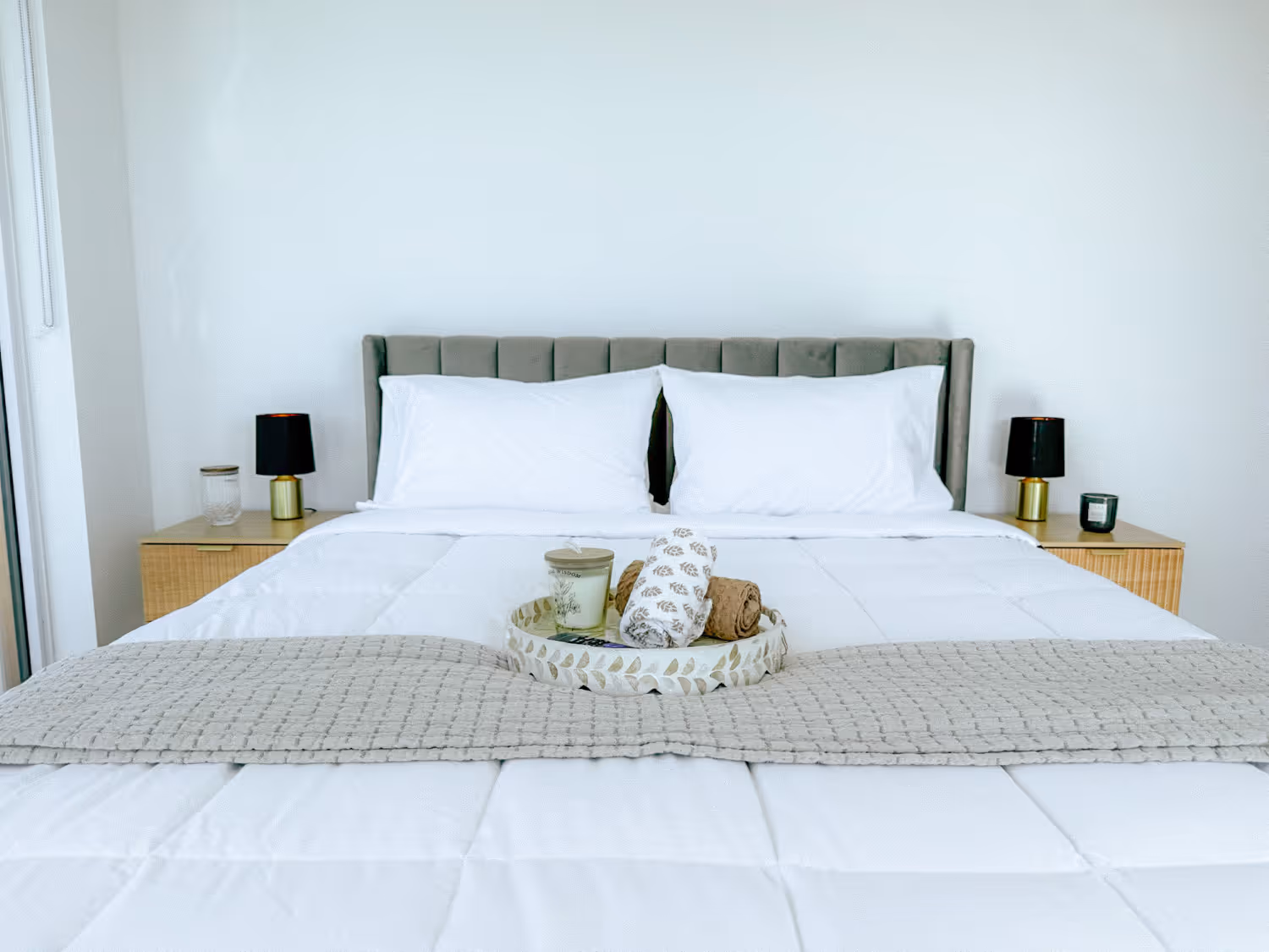 Modern bed with green headboard, white bedding, side tables with black lamps, and decorative tray on bed.