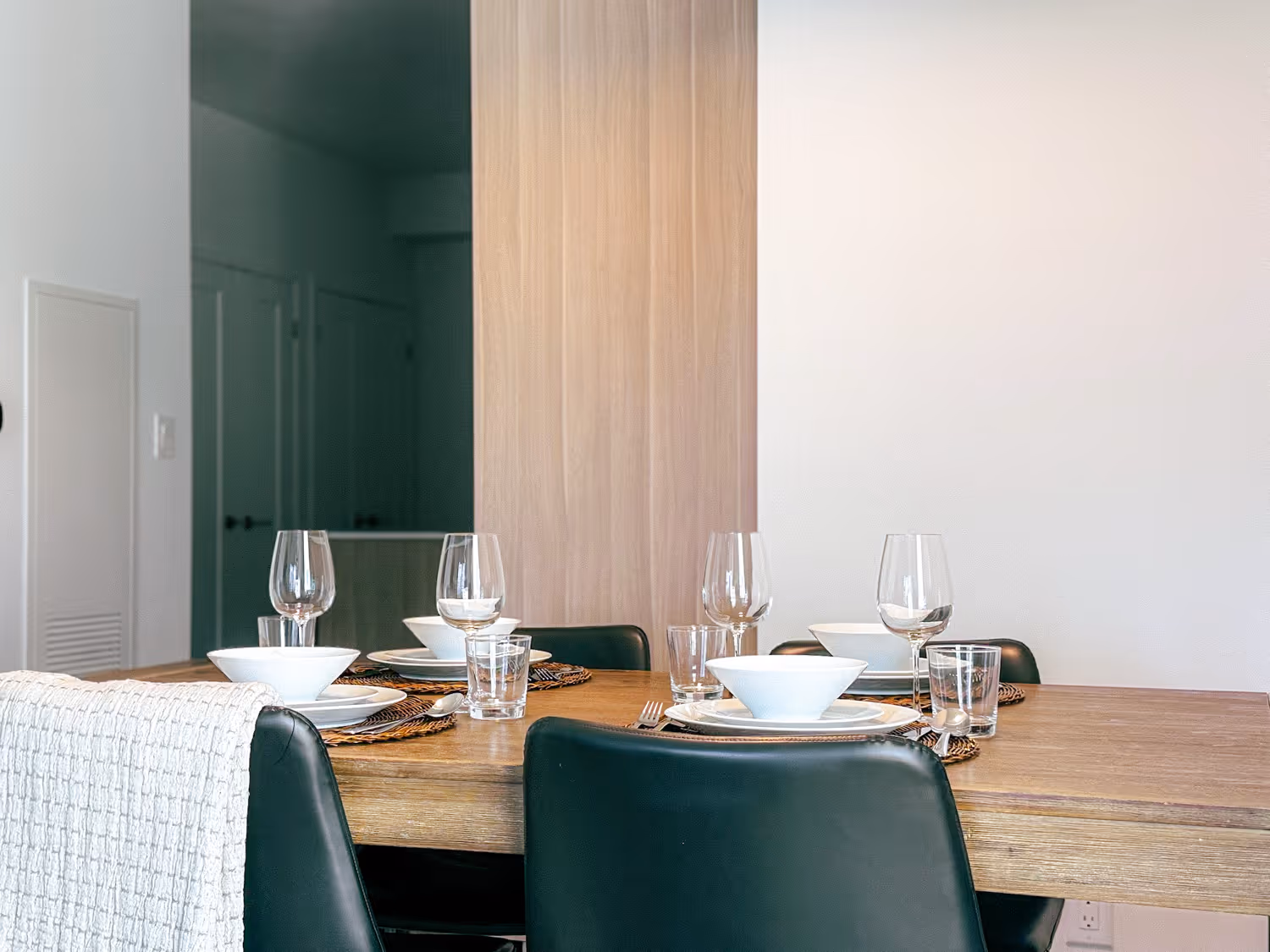 Modern dining table set for four with white bowls, plates, glasses, and black chairs.