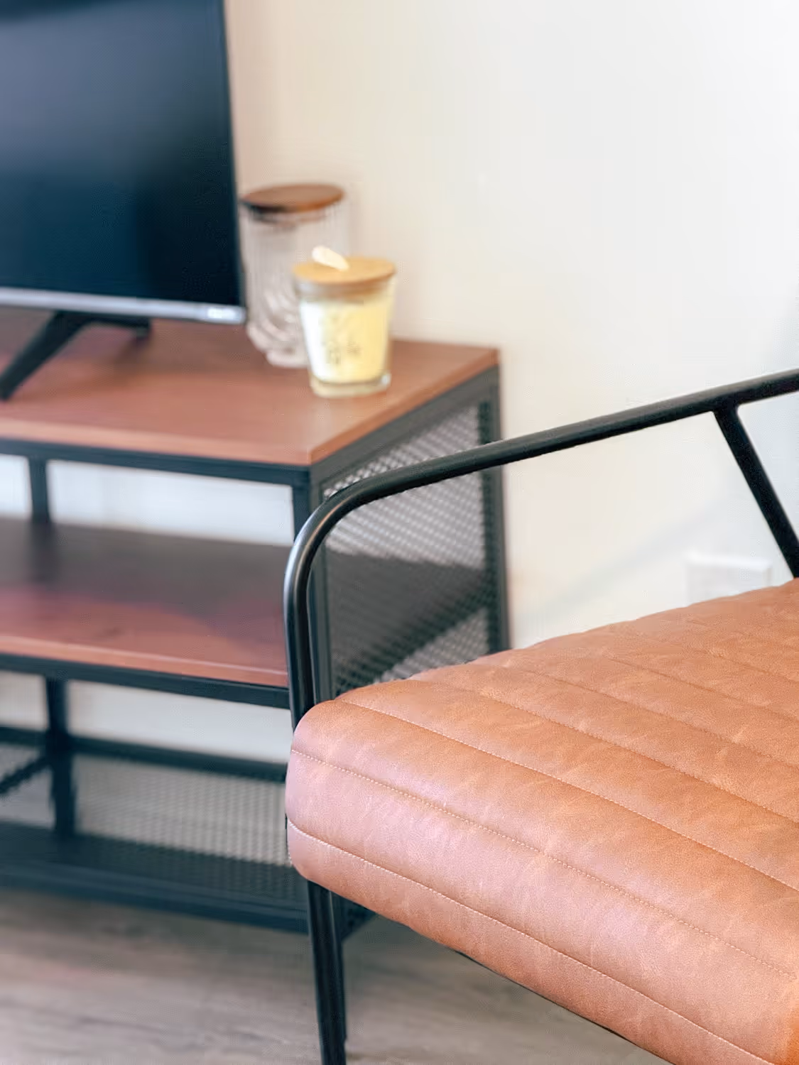 Close-up of a brown leather chair with black metal frame beside a wooden TV stand.