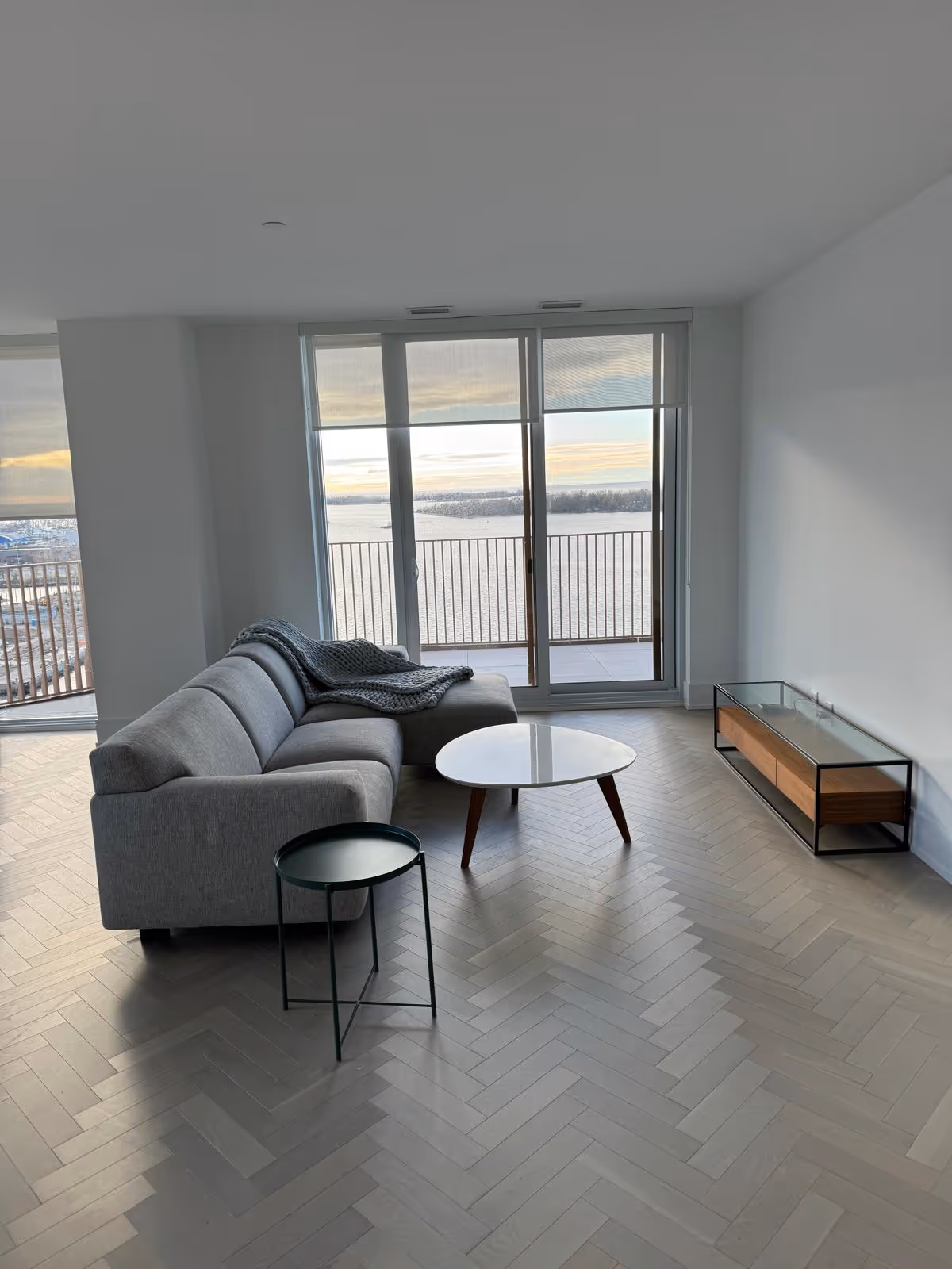 Modern living room with grey sectional sofa, round tables, and large windows overlooking water.